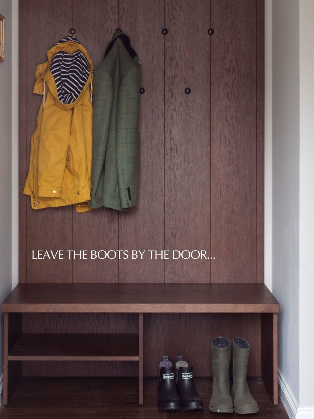 A boot room with jackets on hooks and wellies lined up below, reading Leave The Boots By The Door